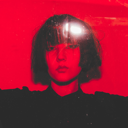 Beautiful asian girl peeking over red plastic filter at the camera so that just her eyes are...