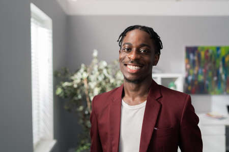 Portrait of an attractive handsome man, standing near a window in a room, dreadlocks on head,...