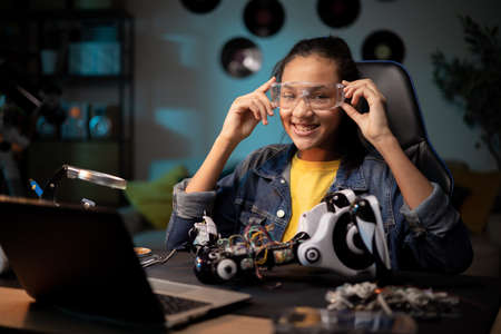 A teenager prepares to fix a toy. She puts on protective goggles for soldering. Girl fixes broken robot, tweaks remote control electronicsの写真素材