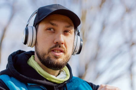 Portrait of a man running in the park and listening to music through wireless headphones. He is...