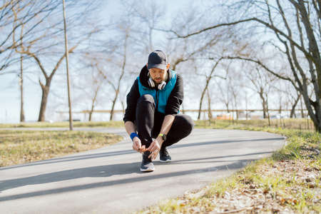 Athlete ties binding sport shoes before jogging. Man running on the street in a city park. Spring...