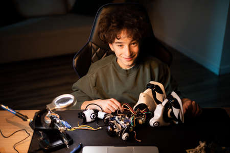 Smiling boy repairs, constructs toy, solders cables, colors wires, smart student develops passion...