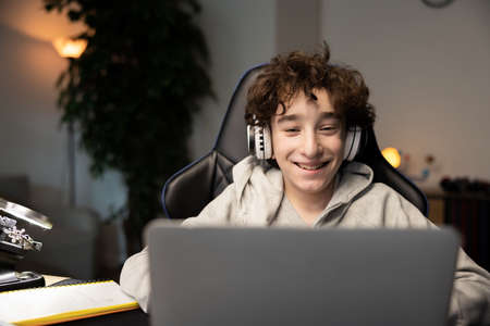 Portrait of happy intelligent young boy smiling at webcam on laptop. Child has remote lessons, video...