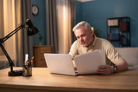 The older man carefully checks the documents. Senior man checks bank statements, pays bills, fees....