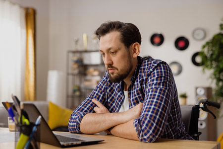 A thoughtful boy sits with his arms folded in front of his computer, contemplating his newly assigned task. The man wonders how best and fastest to complete it.の写真素材