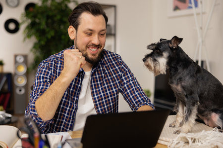 A man with a beard is sitting at a desk with his dog. The brunet in the white blouse is happy, he managed to finish filling out the paperwork. The guy clenches his fist in a gesture of victory.の写真素材