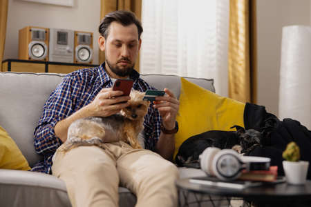 Bruno had forgotten to pay the bill, so he grabbed his smartphone and card and quickly paid the bill. The man also took the opportunity to order food for his pets. Paying bills online.の写真素材