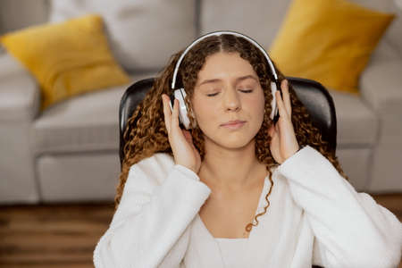 pretty brunette with closed eyes and curly hair, wireless headphones on her ears, which pours her...
