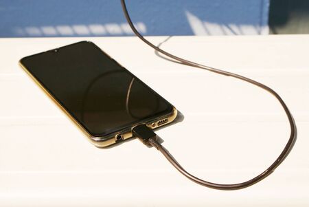 Close up black mobile phone is charging battery on the white table with gray color wall background