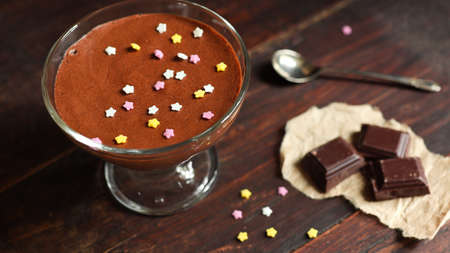 A bowl with chocolate mousse, pieces of dark chocolate and a teaspoon on the old dark brown table backgroundの写真素材