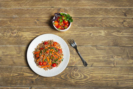 Healthy vegetarian salad with buckwheat and vegetables on a white plate on a wooden background, top view with copy spaceの写真素材