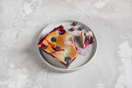 A slice of homemade clafoutis cherry pie - traditional french dessert in a gray plate on a gray...