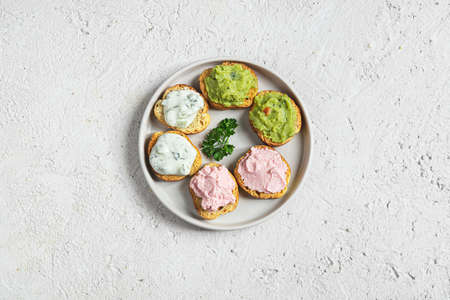 Variety of small sandwiches on the gray plate. Appetizing crostini with tarama, tzatziki and guacamole sauce.の写真素材