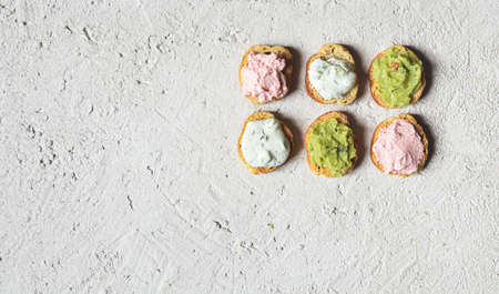 Appetizing crostini or bruschetta with tarama, tzatziki and guacamole sauce. Variety of small sandwiches with various toppings on the gray backgroundの写真素材