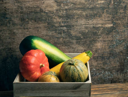 A wooden box with fresh organic vegetables: yellow, green and round zucchini and pumpkin on a wooden background. Harvestingの写真素材