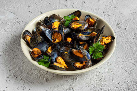 Delicious fresh steamed mussels in white wine sauce with parsley in a white plate on a gray backgroundの写真素材