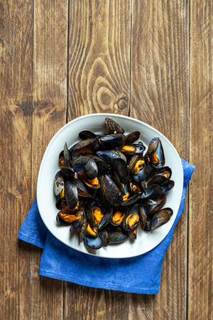 Delicious fresh steamed mussels in white wine sauce with parsley in a white plate on a wooden tableの写真素材