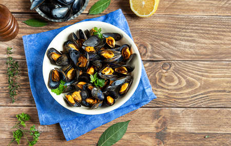 Delicious fresh steamed mussels in white wine sauce with parsley in a white plate on a wooden tableの写真素材