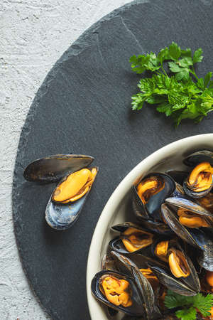 Delicious fresh mussels steamed according to a traditional french recipe in a white wine sauce with parsley in a white plate on a gray backgroundの写真素材