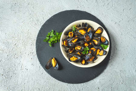 Delicious fresh mussels steamed according to a traditional french recipe in a white wine sauce with parsley in a white plate on a gray backgroundの写真素材