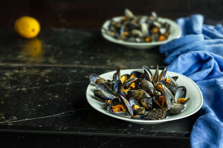 Delicious fresh steamed mussels in white wine sauce in a white plate and a lemon on a dark gray backgroundの写真素材