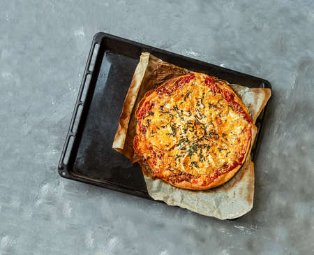 Homemade pizza with bacon, goat cheese and basil on a baking sheet on a gray table. Top viewの写真素材