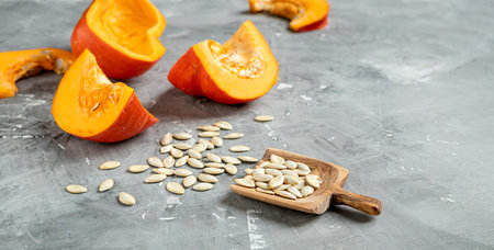 Slices of fresh autumn pumkins and pumkin seeds in a wooden spoon on a gray background with copy spceの写真素材