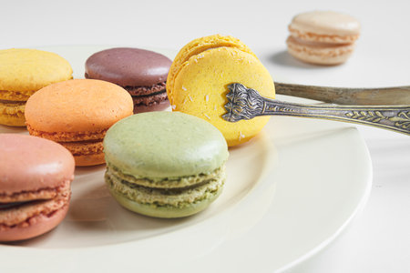 Classic french macaroons of different colors on a light plate and vintage silver serving tongs on a white table, close-upの写真素材