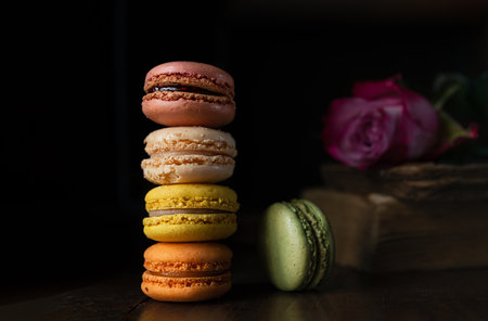 Stack of delicious assorted macaroons of different colors, an old book and a rose on a dark backgroundの写真素材