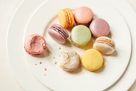 Multicolored delicious french macaroons or macarons lying in a light plate on a white table, top viewの写真素材