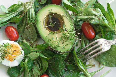 Healthy salad with avocado, egg, lettuce, cherry tomatoes and microgreens in a white plate, top view