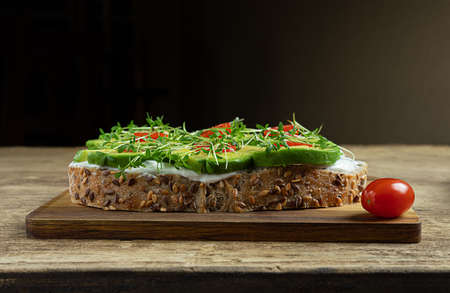 Healthy sandwiches with microgreens - cereal bread toasts with soft cheese, avocado slices, cherri tomatoes and watercress sprouts on a wooden cutting boardの写真素材