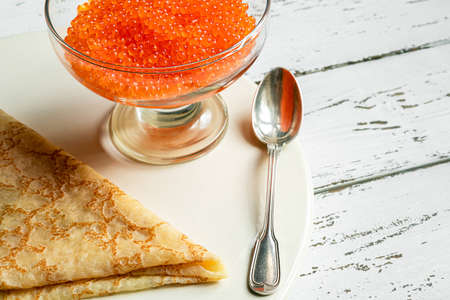 Traditional russian food: pancakes made from wheat flour and red caviar on a white table