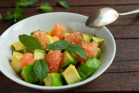 Healthy vegetarian salad with avocado, grapefruit and mint leaves ina white bowl on a dark wooden table close-upの写真素材