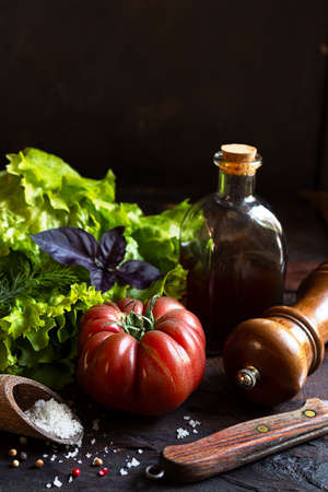 Healthy salad ingredients - fresh organic lettuce and tomatoes, a bottle with vegetable oil and spices on an old wooden table, low key photoの写真素材