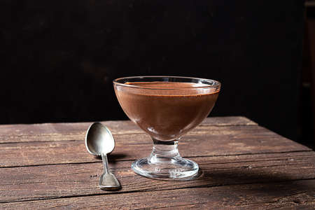 A bowl with traditional chocolate mousse and a spoon on dark wooden background
