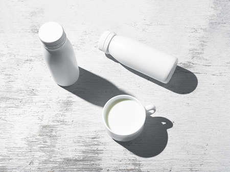 White cup and white botlles with milk or dairy product on white wooden background, diet and healthy...