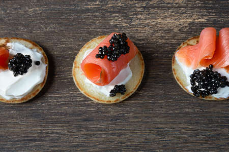 Blini pancakes with black sturgeon caviar and salmon on a wooden tableの写真素材