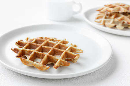 Waffles on white plates close-up and a cup of milk on a white table, tasty breakfast conceptの写真素材