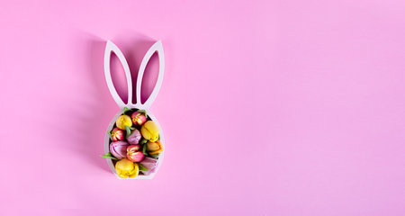 Wooden easter bunny statuette with spring tulips on the pink background, easter minimal concept, top view with copy spaceの写真素材