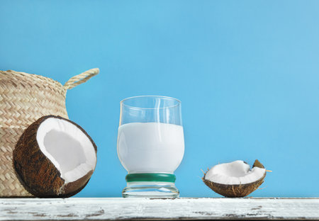 A glass of coconut milk cocktail and a coconut on a light blue background, summer organic vegan beverageの写真素材