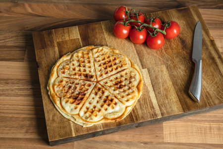 Pizza waffle with pepperoni, olives and parmesan cheese and cherry tomatoes on a cutting board on the kitchen tableの写真素材