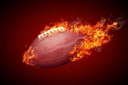 American football ball in fire isolated on dark red backgroundの写真素材