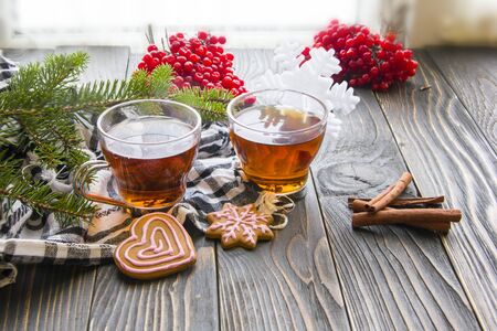 Cup of tea, fir branch, red berries, ginger cookies and cinnamon on wooden tableの写真素材