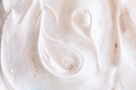 Creamy texture of white airy scrub foam with peeling particle. Cosmetic background with warm light bege hueの写真素材