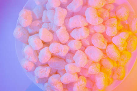 Corn sticks in sugar powder. Sweet food background. Corn sticks in mixed colorful creamy pink and yellow light. Crispy, sweet and fun snack for party and movie timeの写真素材