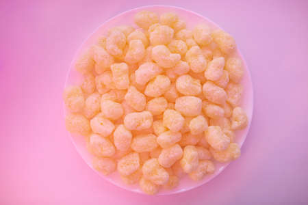 Corn sticks in sugar powder on a plate. Sweet food background. Yellow crispy corn sticks on light pink background. Sweet and fun snack for party and movie timeの写真素材