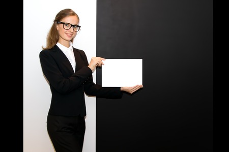 The girl wearing eyeglasses with a blank sheet in hands costs at a black-and-white wallの写真素材