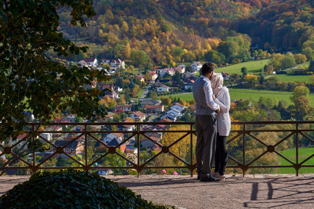 A couple in love stands at the fence and admires the beautiful view of the valleyの写真素材