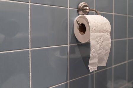 Roll of toilet paper on metal paper holder. Bathroom tissue hanging on the wall. Soft white toilet paper on tiled background.の写真素材